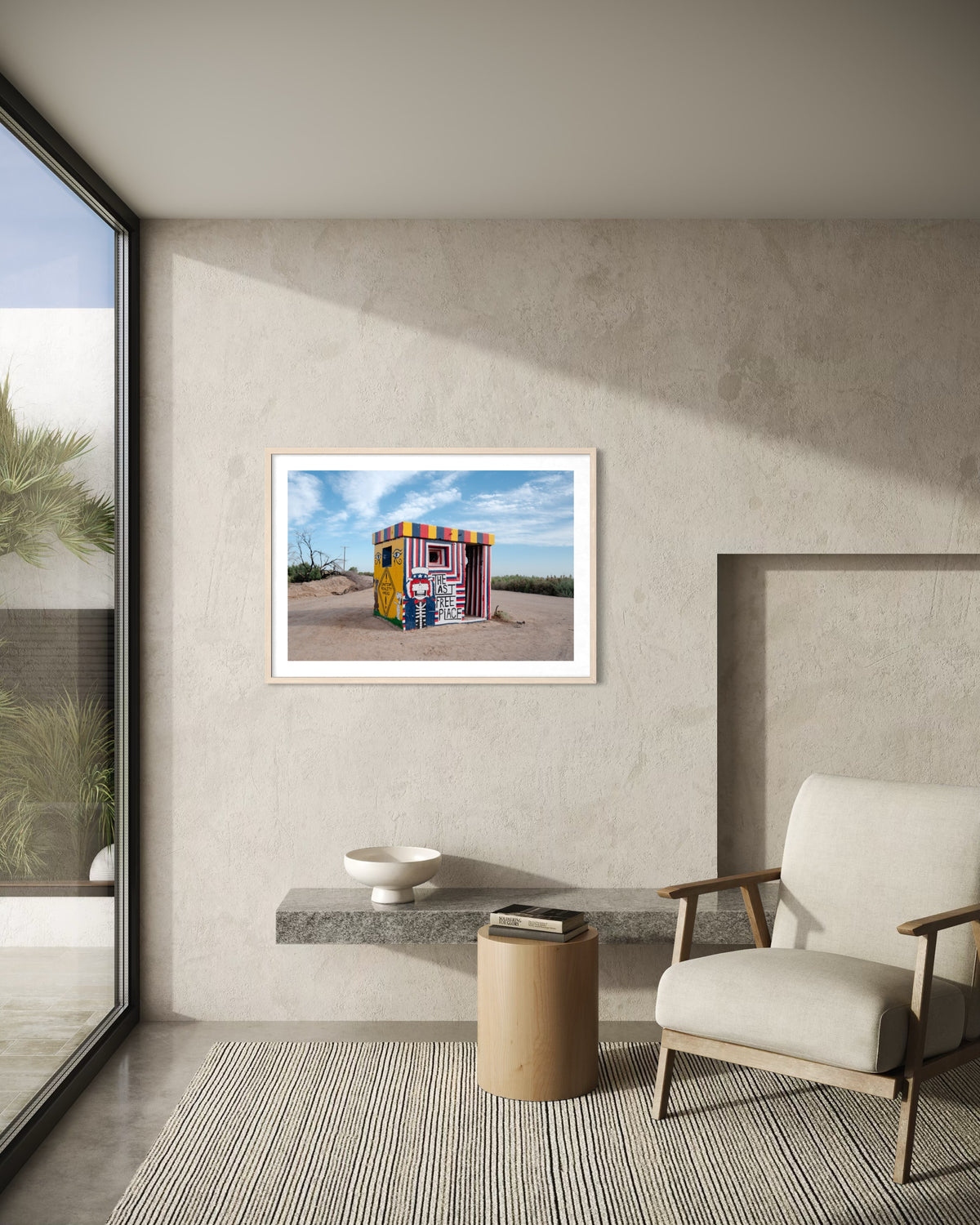 Beige living room with a modern chair and “The Last Free Place” artwork photographed in Slab City, California.