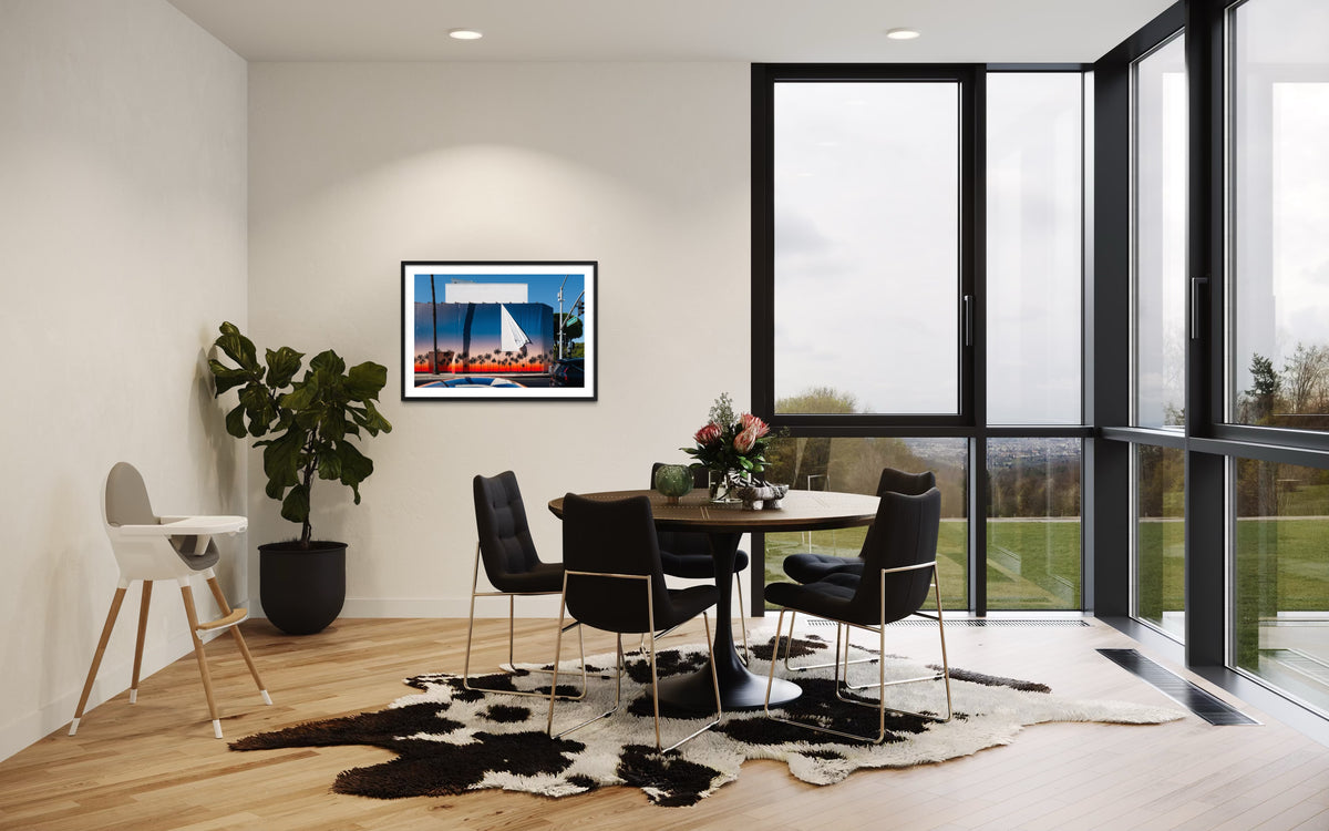 Black chairs and round table on cowhide rug, Beverly Hills wall art, large windows in a dining area.