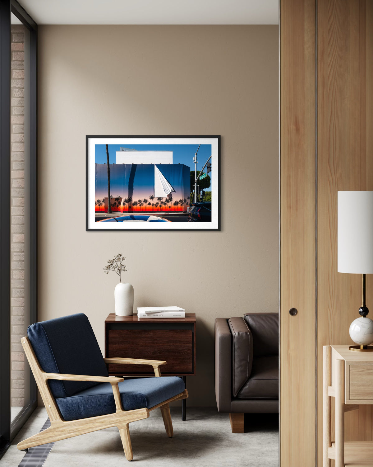 Navy chair and brown sofa in a living room, “Beverly Hills Revealed” artwork on the wall.