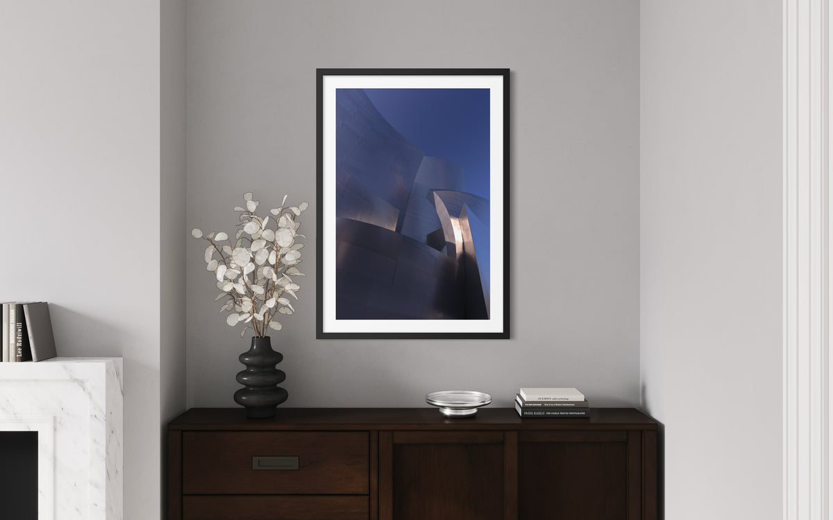 Abstract Blue Gehry building photo, framed and displayed on a gray wall above a dark wood cabinet with decor.