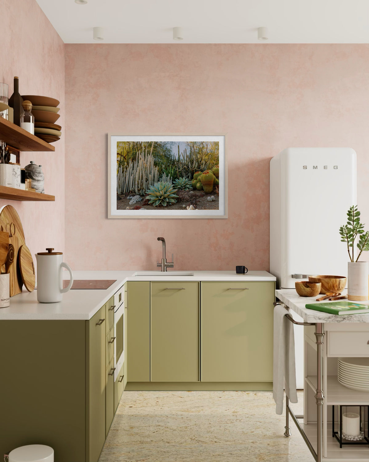 Green kitchen cabinets, pink walls, white SMEG fridge, and Cactus Garden I art above the sink.