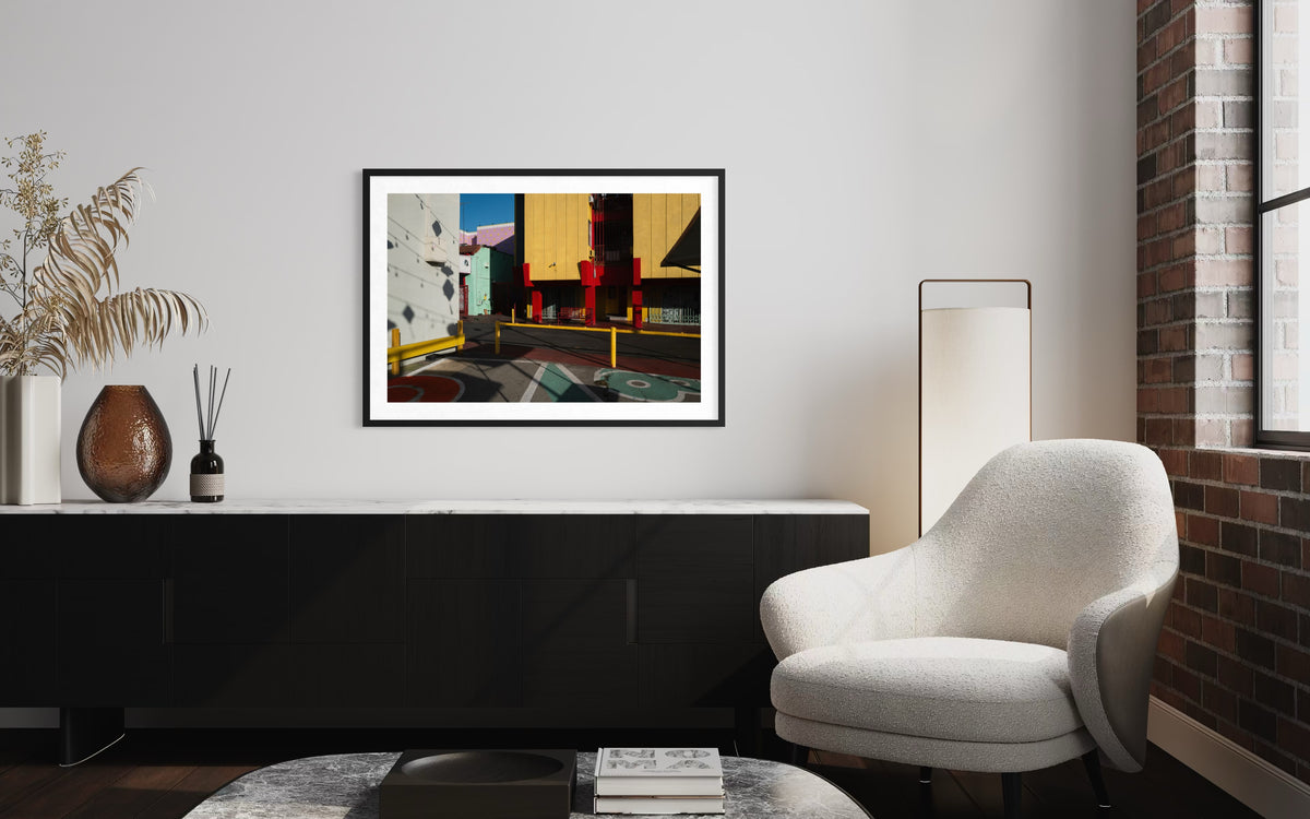 White chair, lamp, and Chinatown Study artwork above a black sideboard in a modern living room setting.