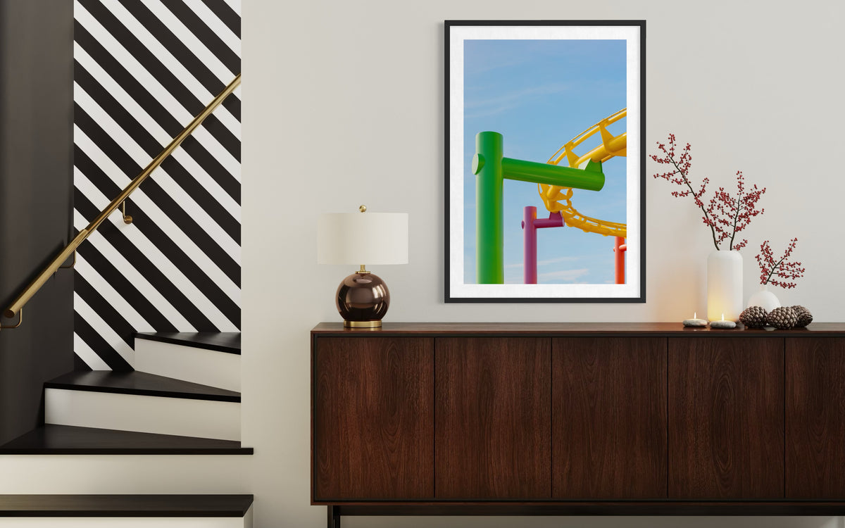 Striped staircase, sideboard, lamp, and framed Coaster Colors roller coaster photos in a modern hallway.
