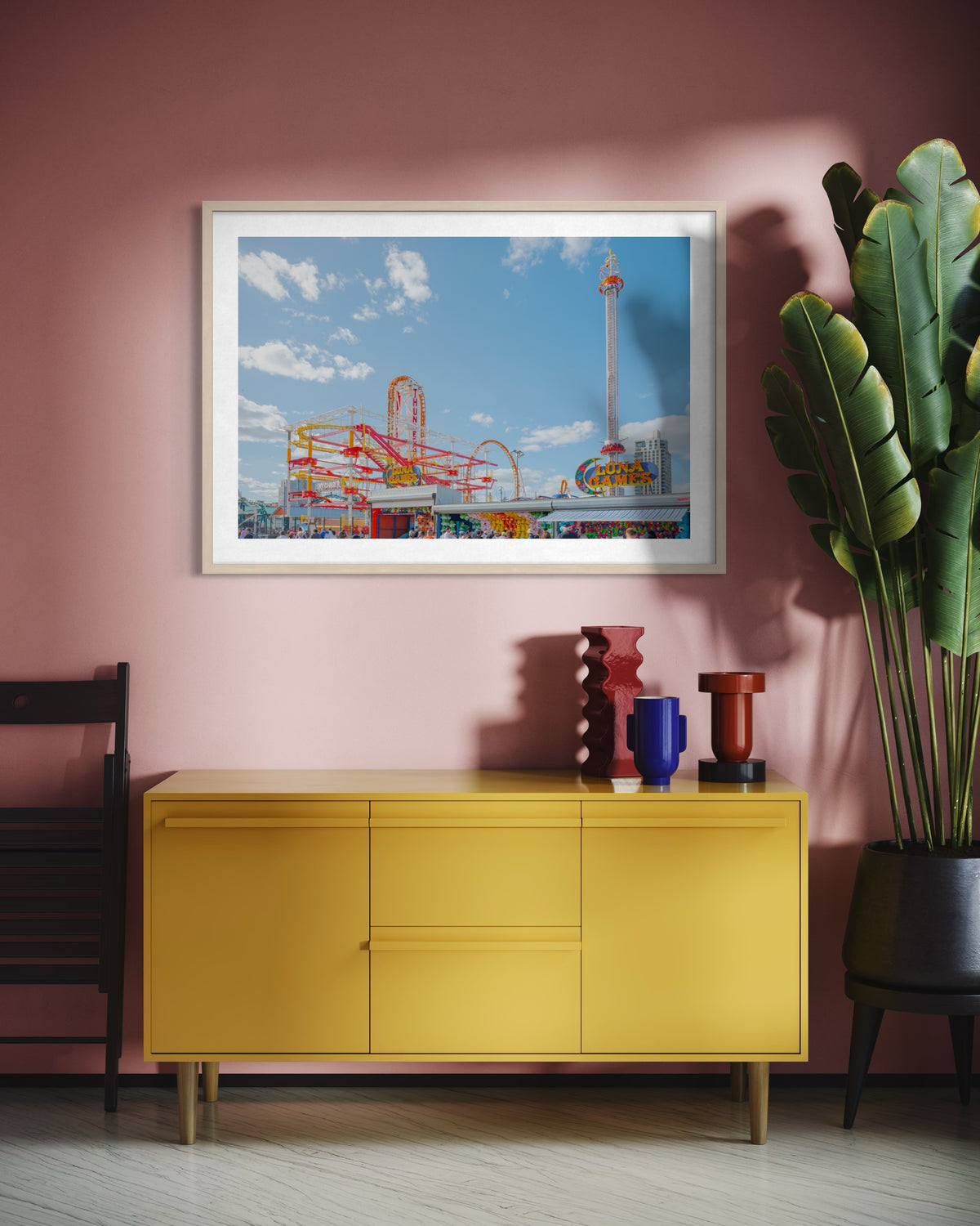 Yellow sideboard below framed “Coney Island Luna Games” print on a pink wall with plants and decor.