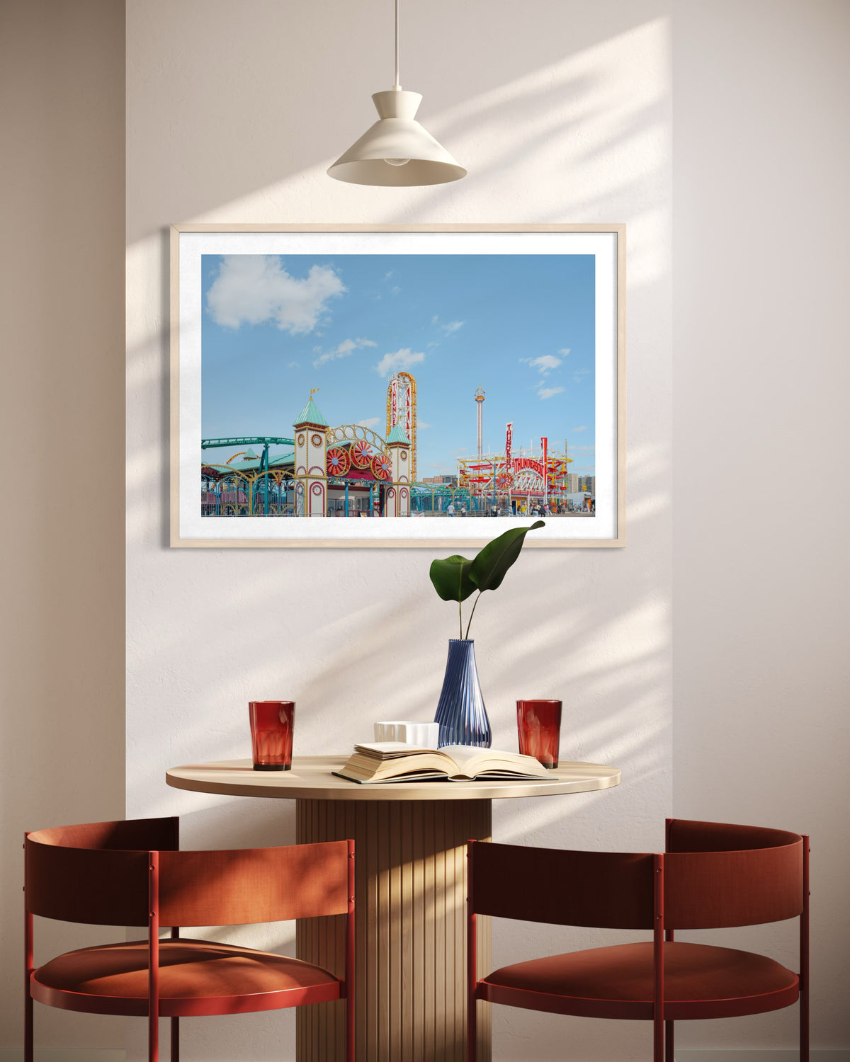 Two red chairs and a round table with books below a “Coney Island Thunderbolt” sign on a white wall.