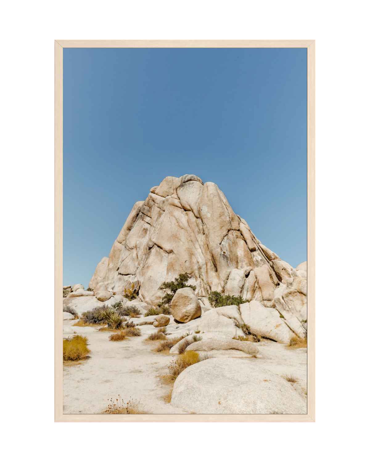 Large desert rock formation under clear blue sky, surrounded by sand and sparse vegetation in a dry landscape.