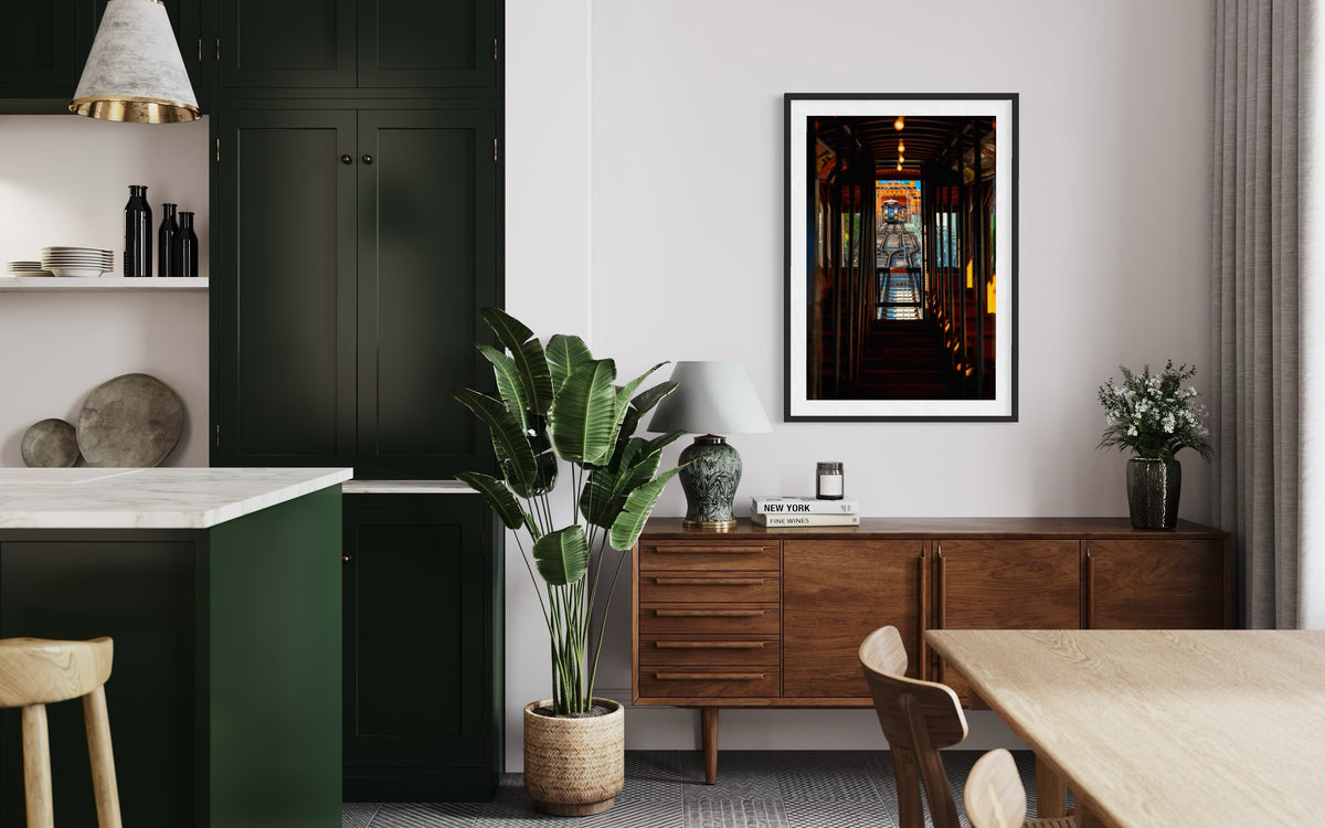 Green cabinets and a potted plant in a dining room, with DTLA Funicular art above the sideboard in Los Angeles.