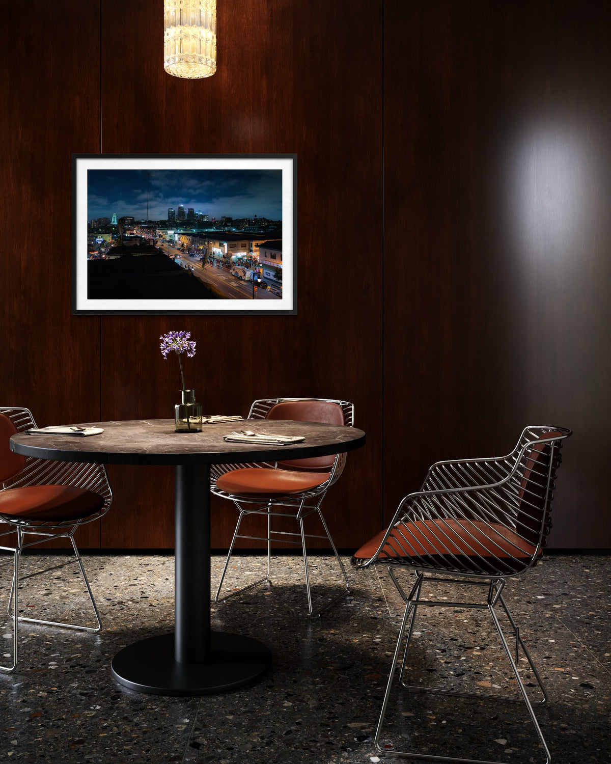 Round table with four metal chairs and orchid centerpiece, Downtown Los Angeles cityscape photo in background.