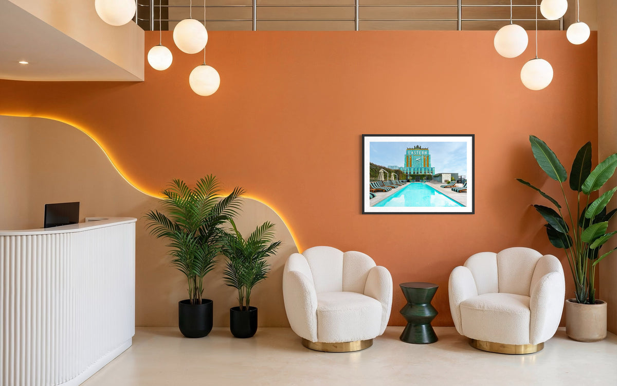Orange-walled lounge with two white chairs, plants, and framed Eastern Columbia Building photo from Los Angeles.