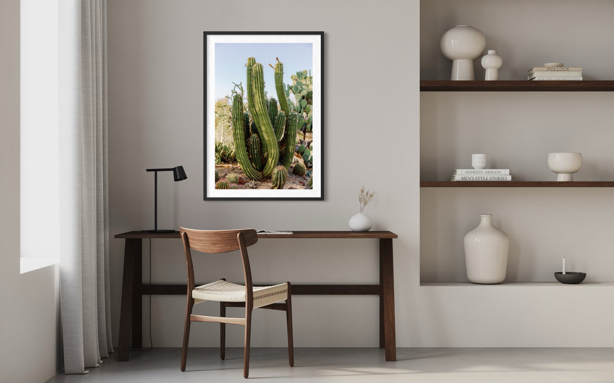 Framed Elephant Cactus photo hangs above a wooden desk with shelving in a minimalist workspace setting.