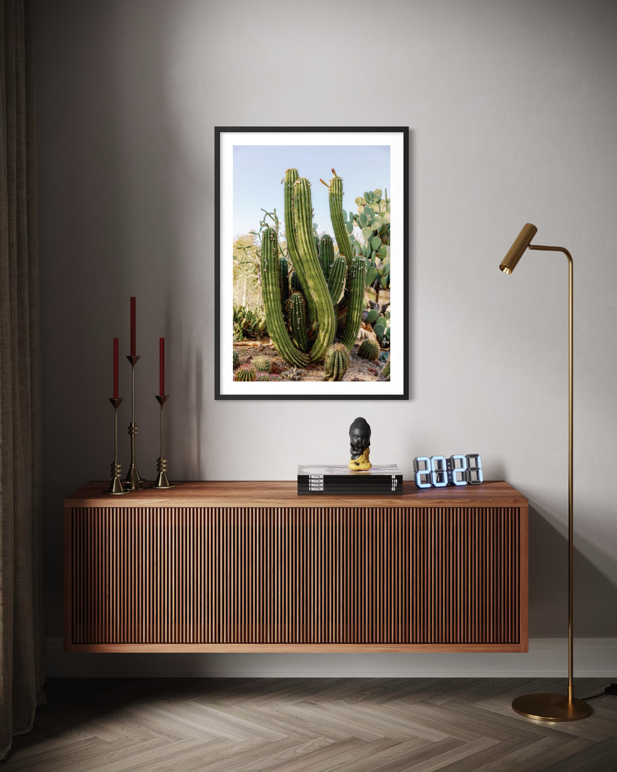 Framed photo of an Elephant Cactus hangs above a console with candles, a bust, books, and gold floor lamp.