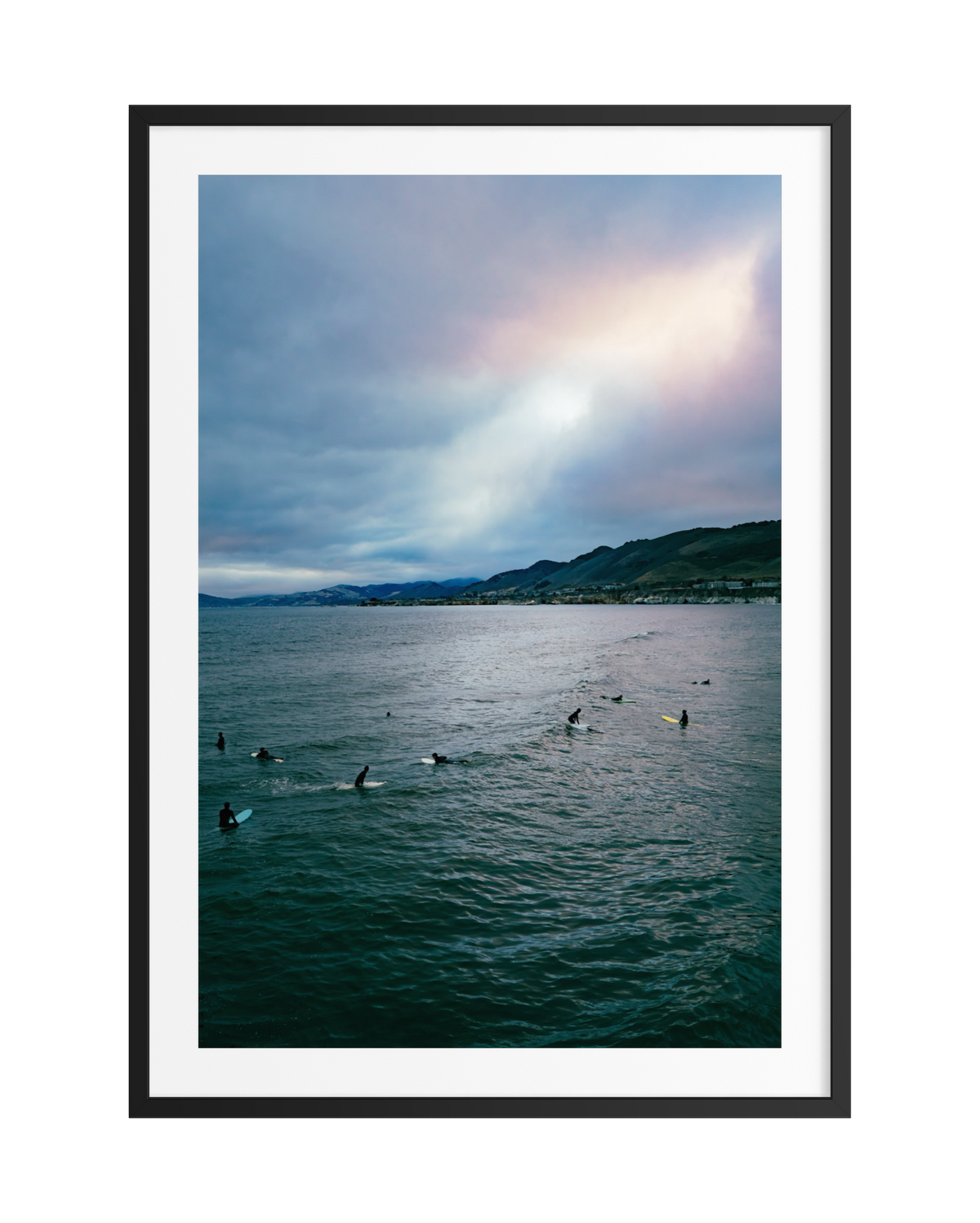Surfers sit on boards in the ocean at sunset near Pismo Beach, California.