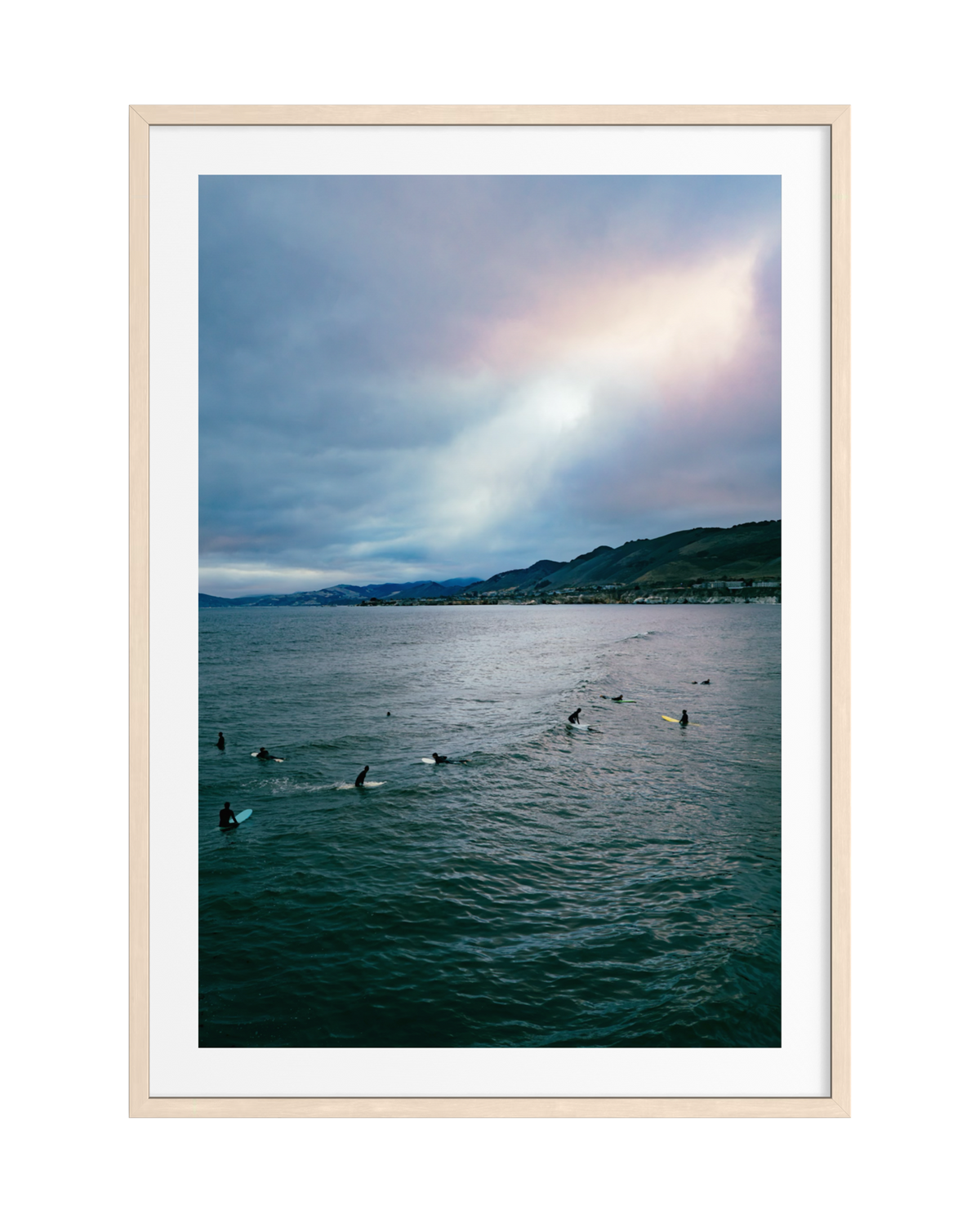 Surfers float on the water at sunset off Pismo Beach under a colorful sky.