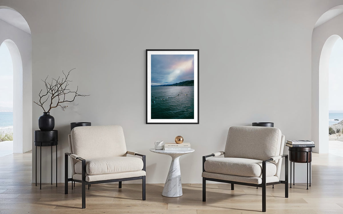 Framed Ethereal Sky Pismo Beach print on wall, two beige armchairs, marble table, and arched windows in view.
