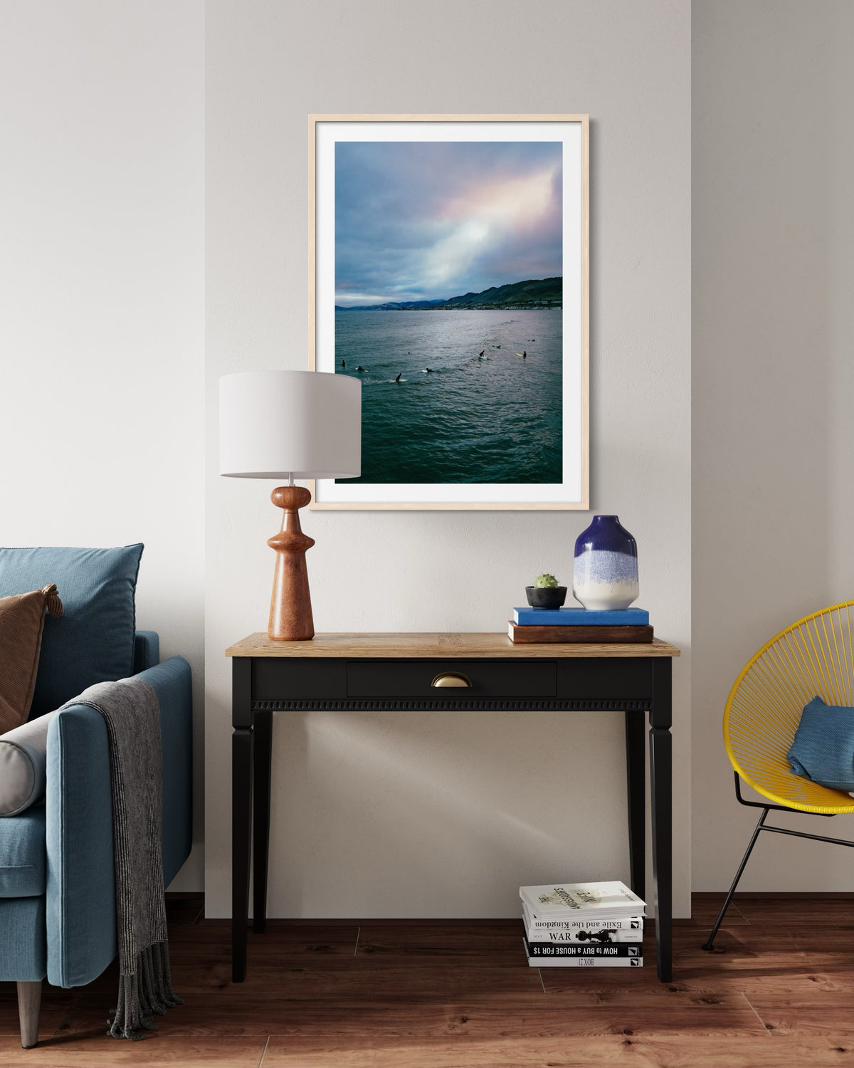 Framed print of Pismo Beach sky hangs above a wooden desk with lamp, blue vase, books, and a chair.