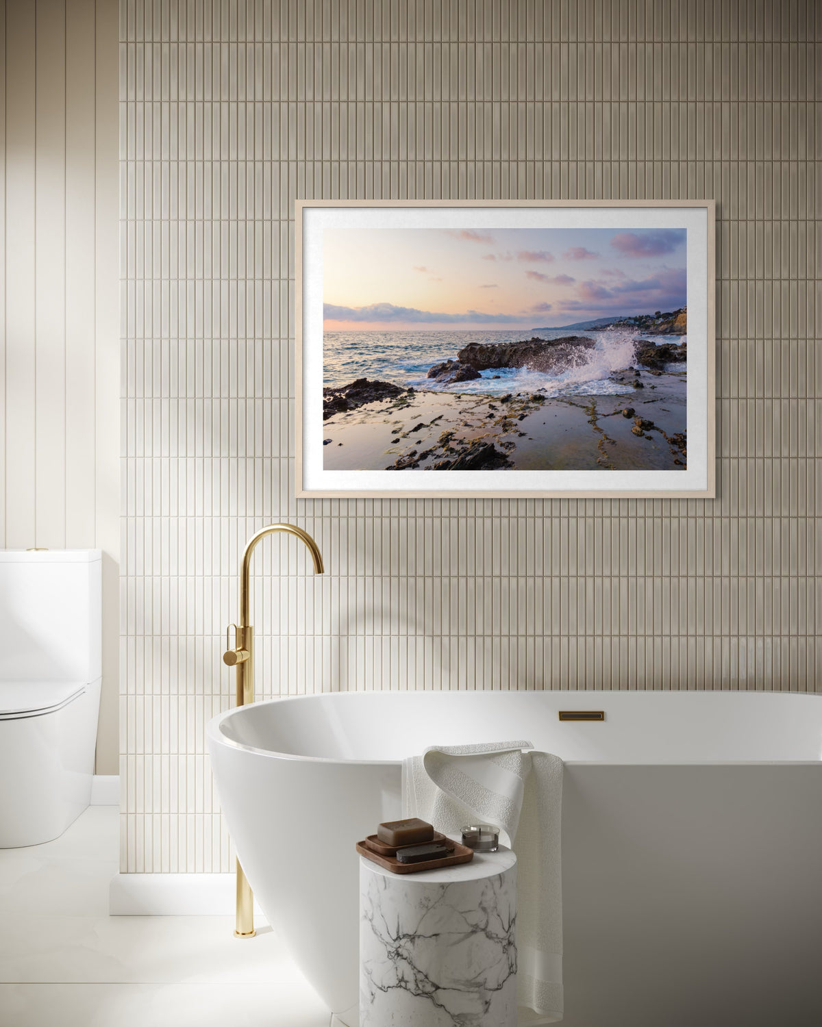 Freestanding tub with gold faucet beneath the Evening Splash artwork in a Laguna Beach bathroom setting.