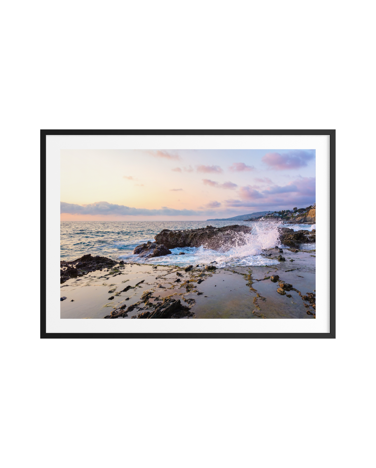 Waves crash at sunset on Laguna Beach, ocean spray rising beneath pastel skies and scattered clouds.