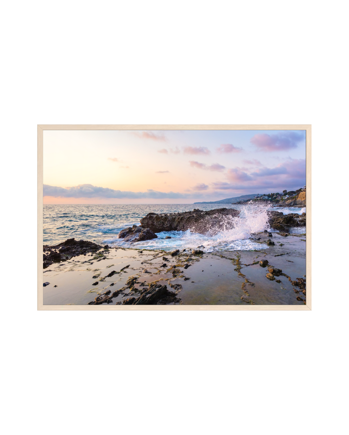 Waves crash against Laguna Beach rocks at sunset, soft pastel clouds above a calm summer ocean.