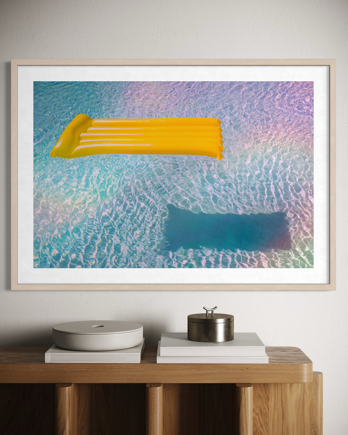 Yellow pool float drifts on blue water; framed photograph displayed above a wooden cabinet.