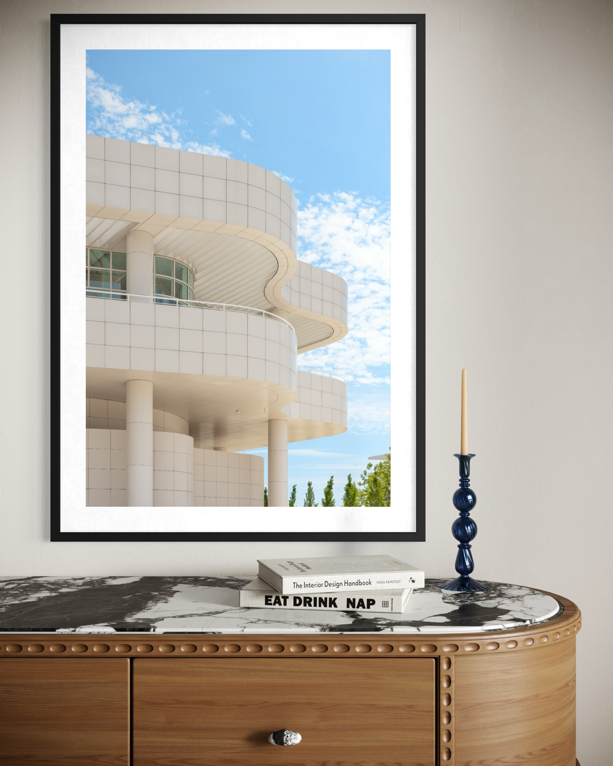 Getty Center Los Angeles print in black frame above a marble dresser with books and blue candle holder.