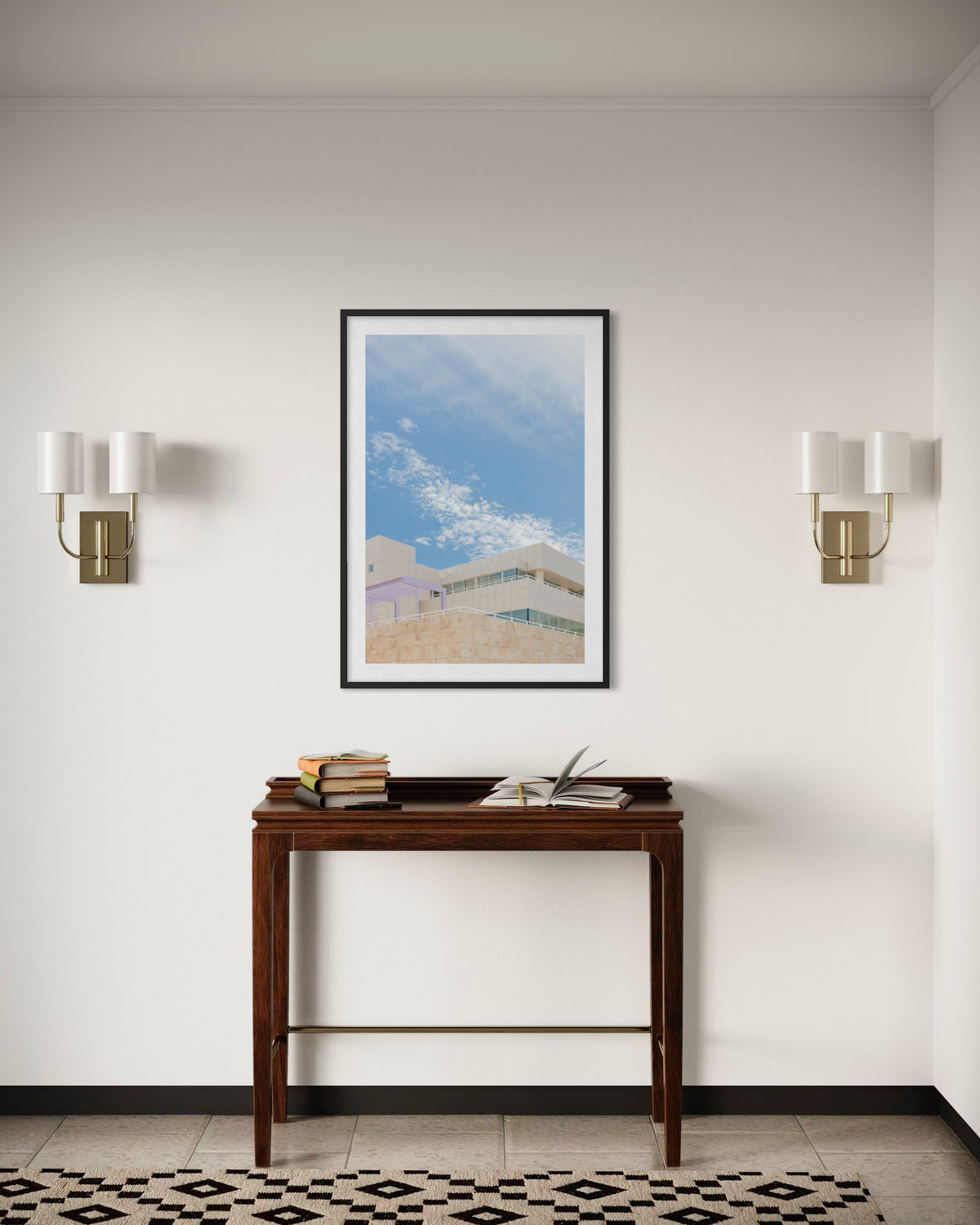 Framed Getty Center II Los Angeles print displayed above console table with books and two wall sconces.