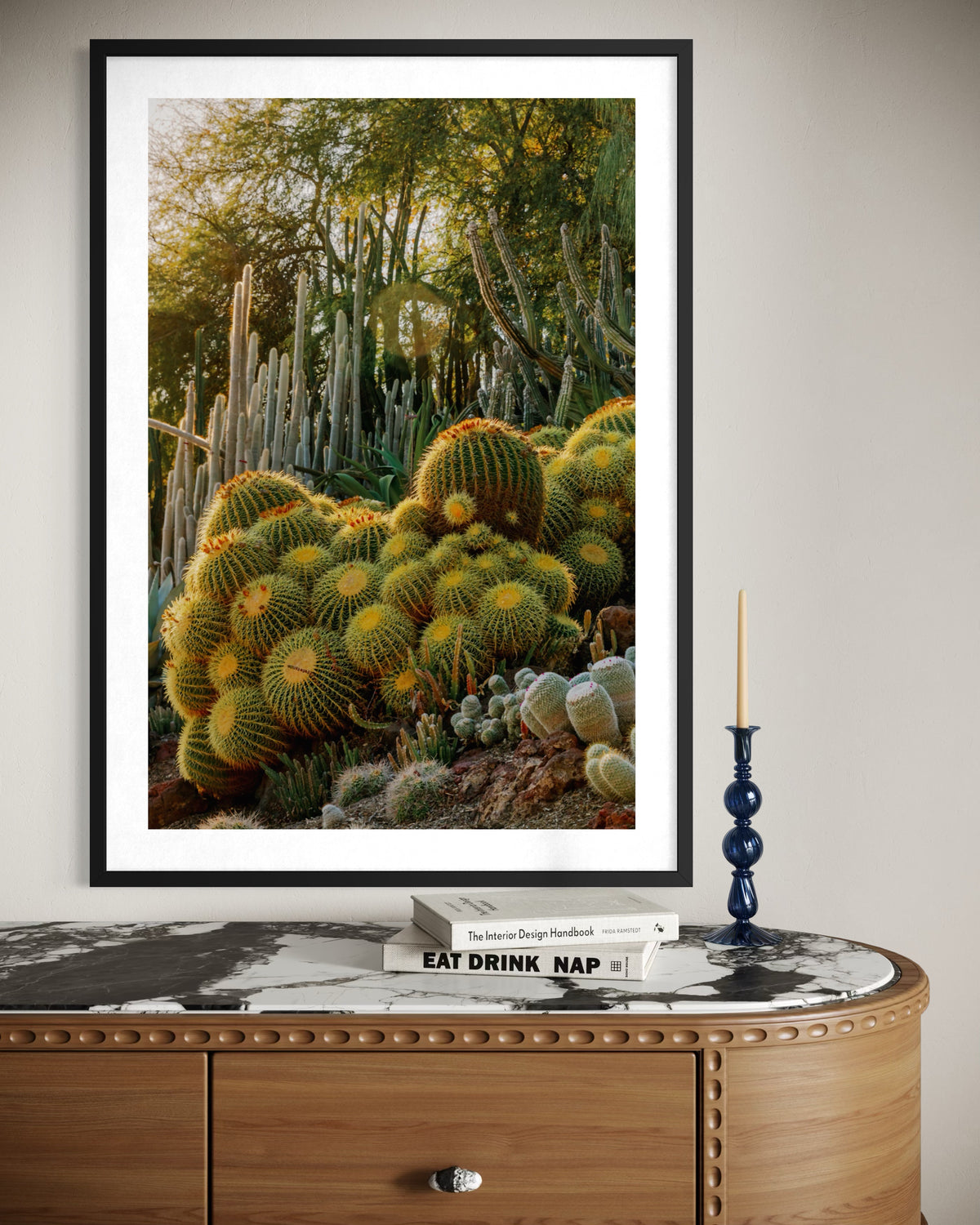 Golden Barrel Cactus photograph above a marble-top dresser with books, a blue candleholder, and a single candle.