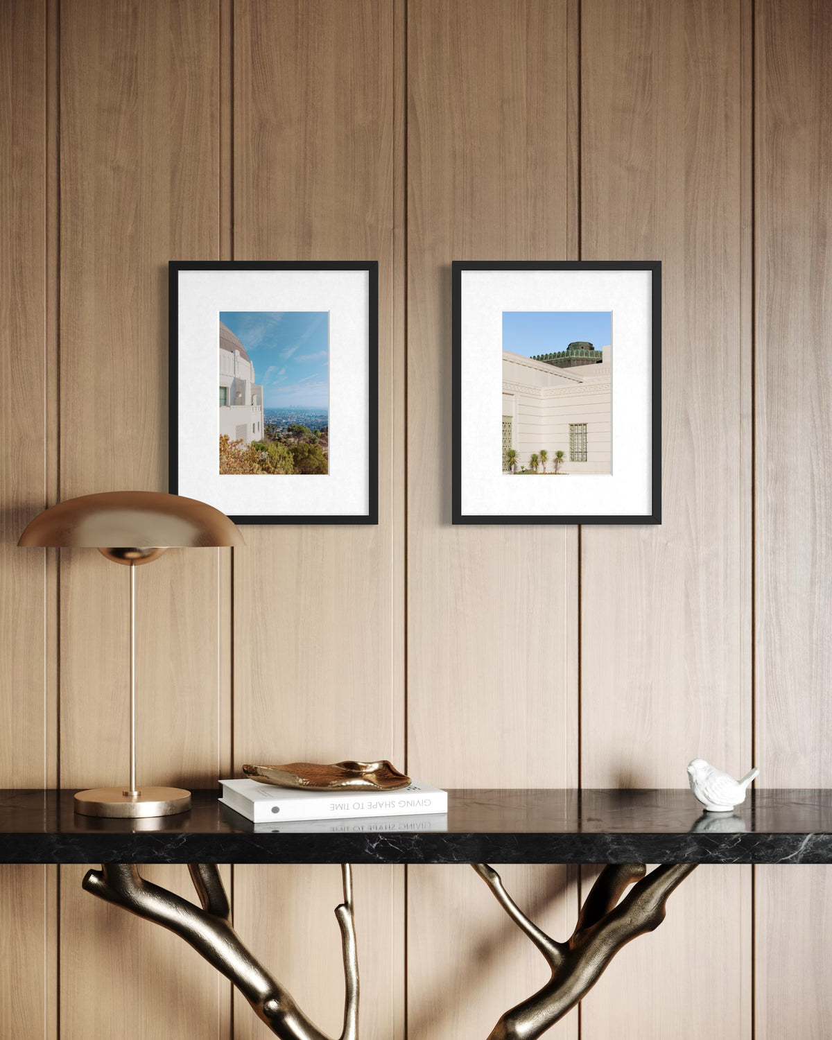 Framed Griffith Observatory photograph above a wood-paneled wall, with console table, books, and lamp below.