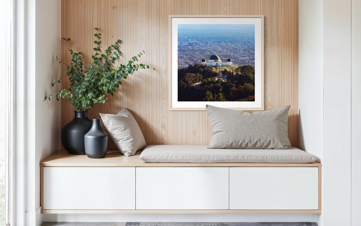 Griffith Observatory in Los Angeles against a wood wall, with black vases and a gray pillow on a built-in bench.