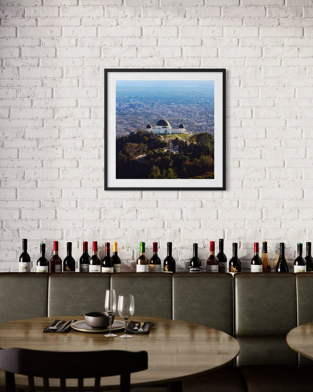 Griffith Observatory photograph hangs above bottles on set tables against a white brick wall in Los Angeles.