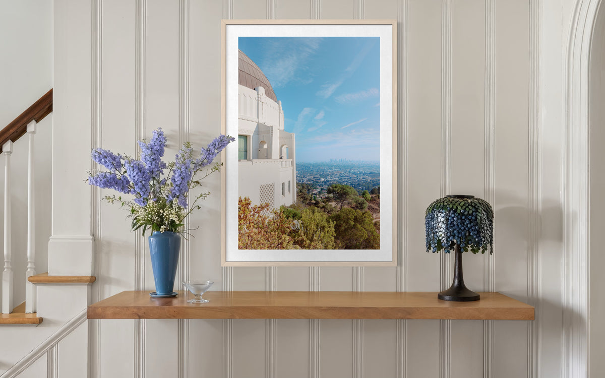 Framed print of Griffith Observatory, Los Angeles, displayed above a wood shelf with flowers and a lamp.