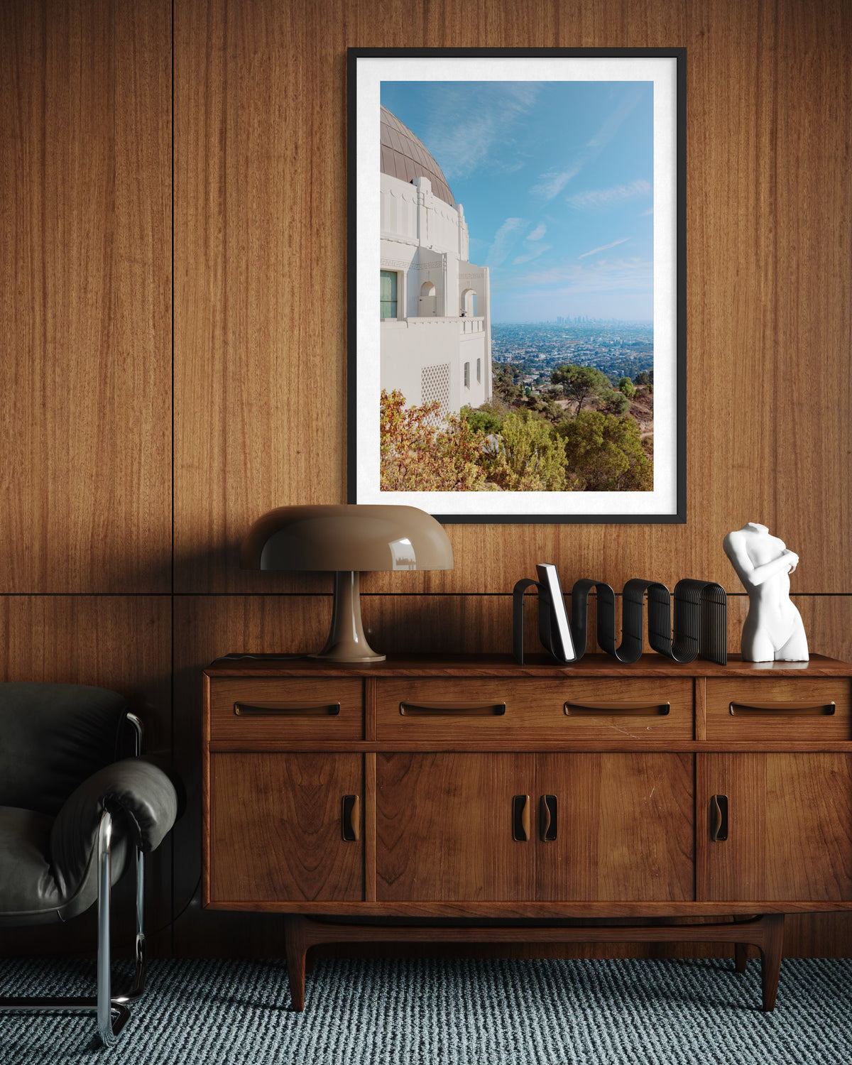 Framed Griffith Observatory View art hangs on a wood-paneled wall above a wooden sideboard with decor.