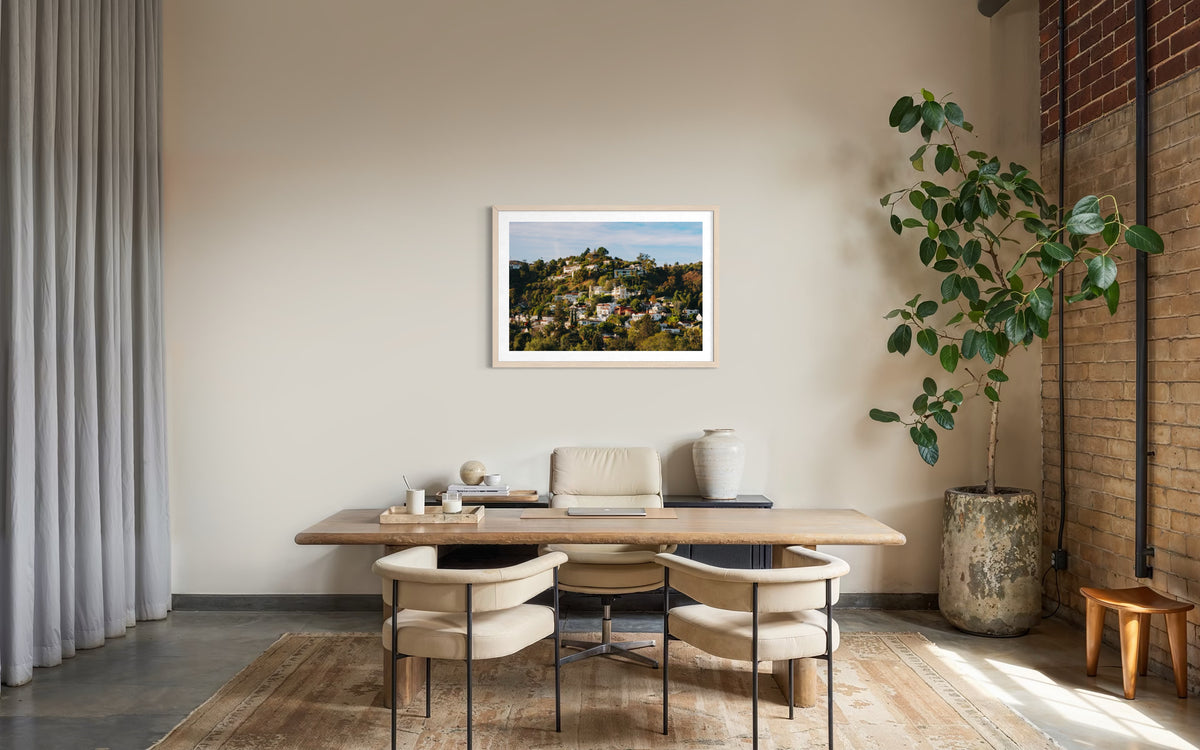 Modern home office with wooden desk, two chairs, and framed Hollywood Hills photograph on the wall.