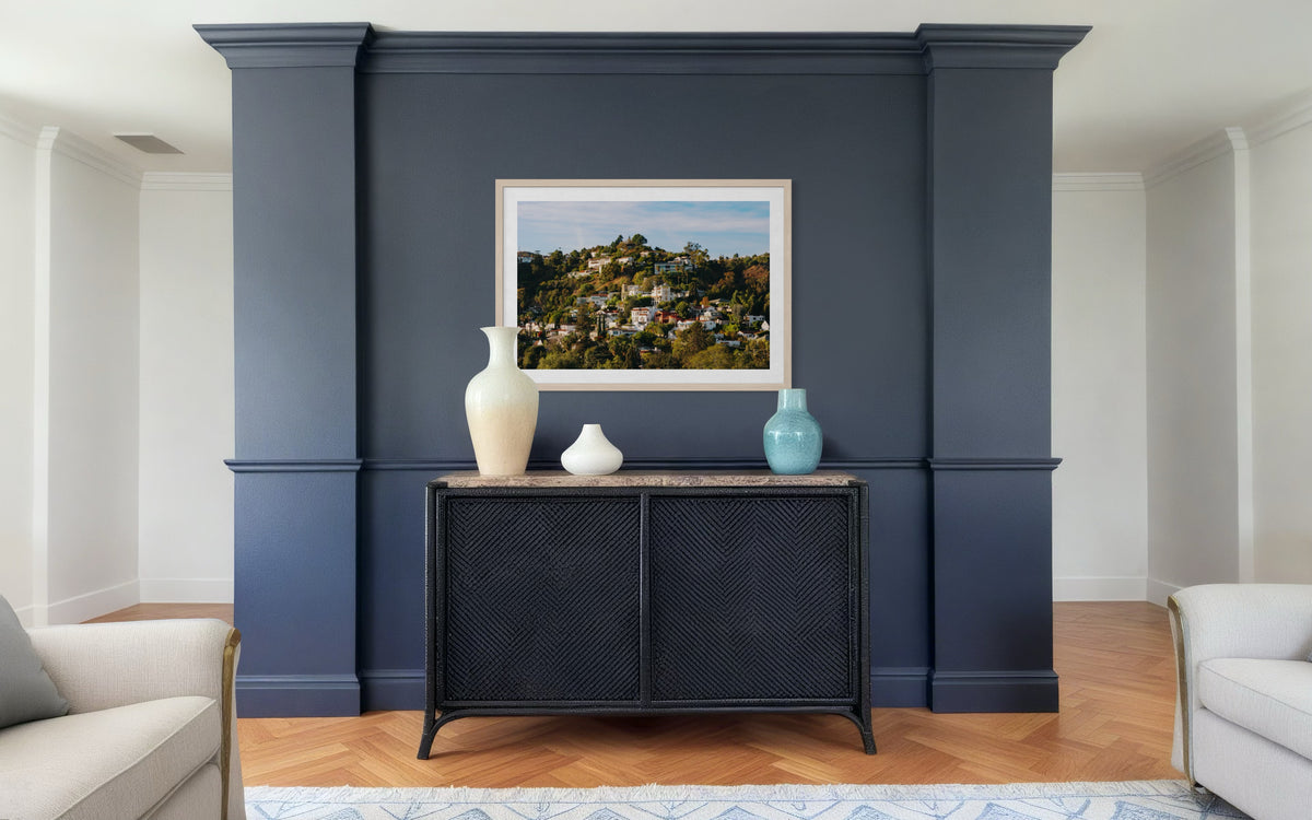 Black console with vases sits below framed “Hollywood Hills” art against a navy wall.