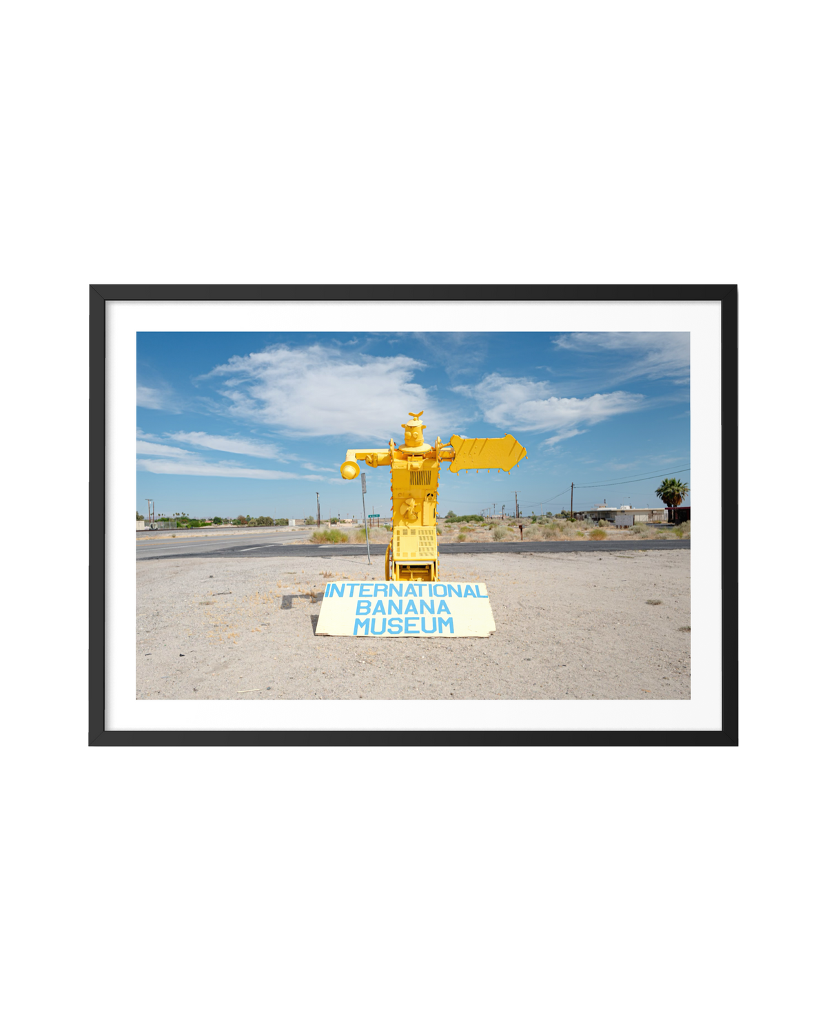 A yellow robot near the International Banana Museum sign in the Salton Sea desert under a blue sky.