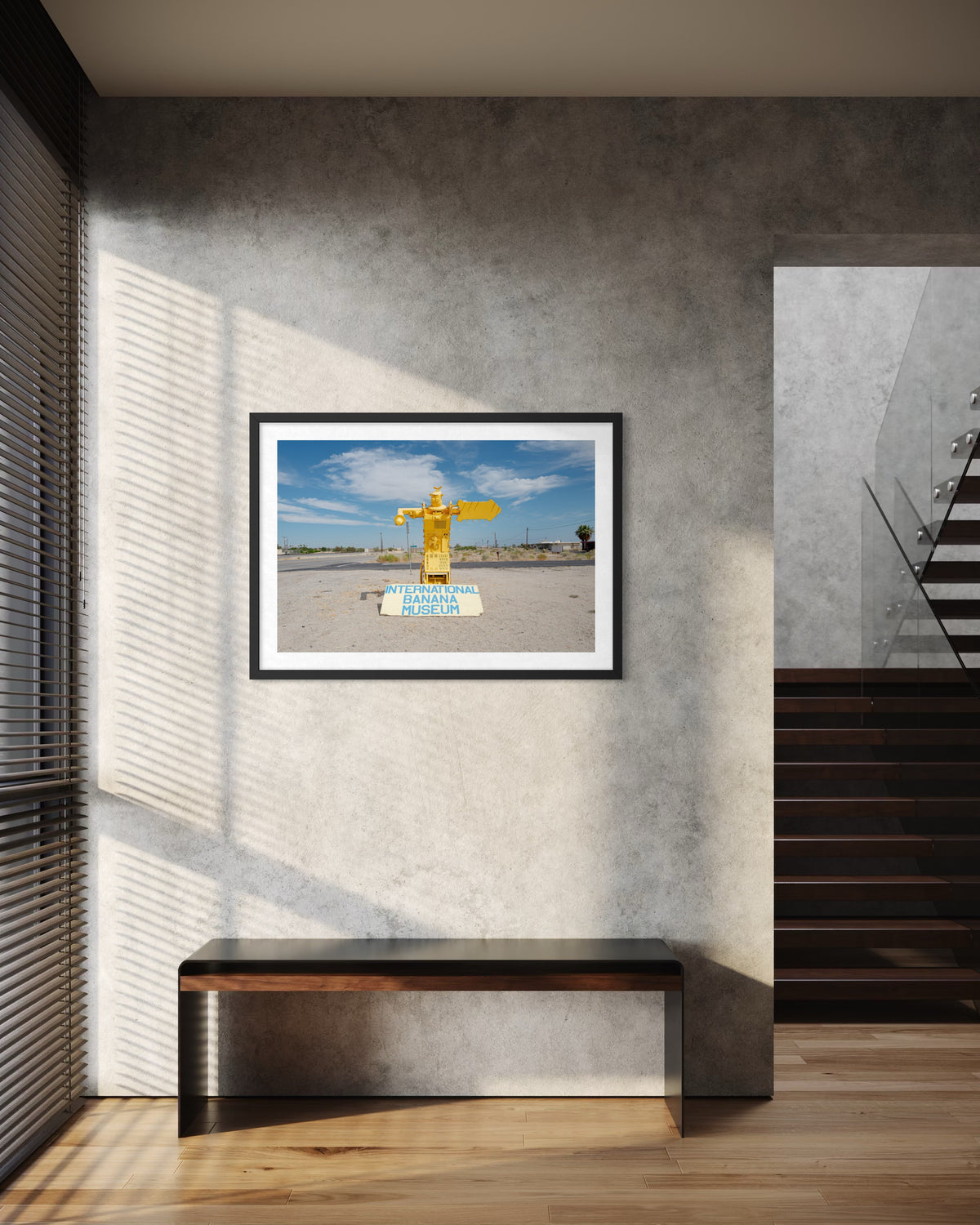Framed “International Banana Museum” photograph above a bench on a gray wall in a modern hallway.