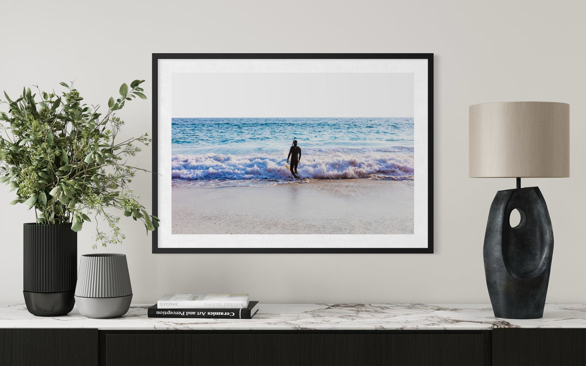 Framed print of a lone figure standing on the beach, titled “Into The Sea,” displayed above a marble console.