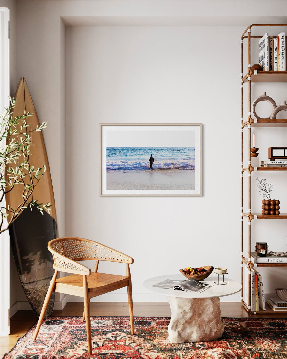 Framed “Into The Sea” surf photo displayed in a modern living room with surfboard, chair, bookshelves, and plants.