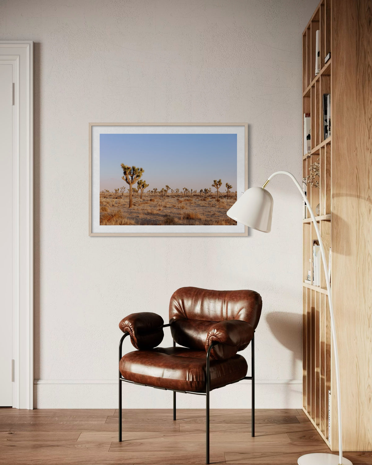 Framed “Joshua Tree Evening” photo above a brown leather chair, lamp, and shelf in softly lit room.