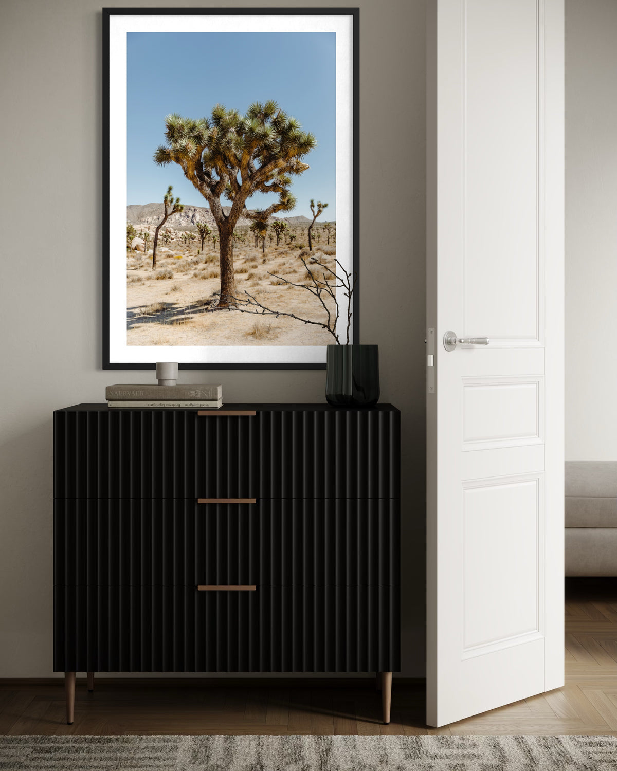 Framed “The Joshua Tree I” print depicting Joshua Tree, California, above a black dresser with books and a vase.