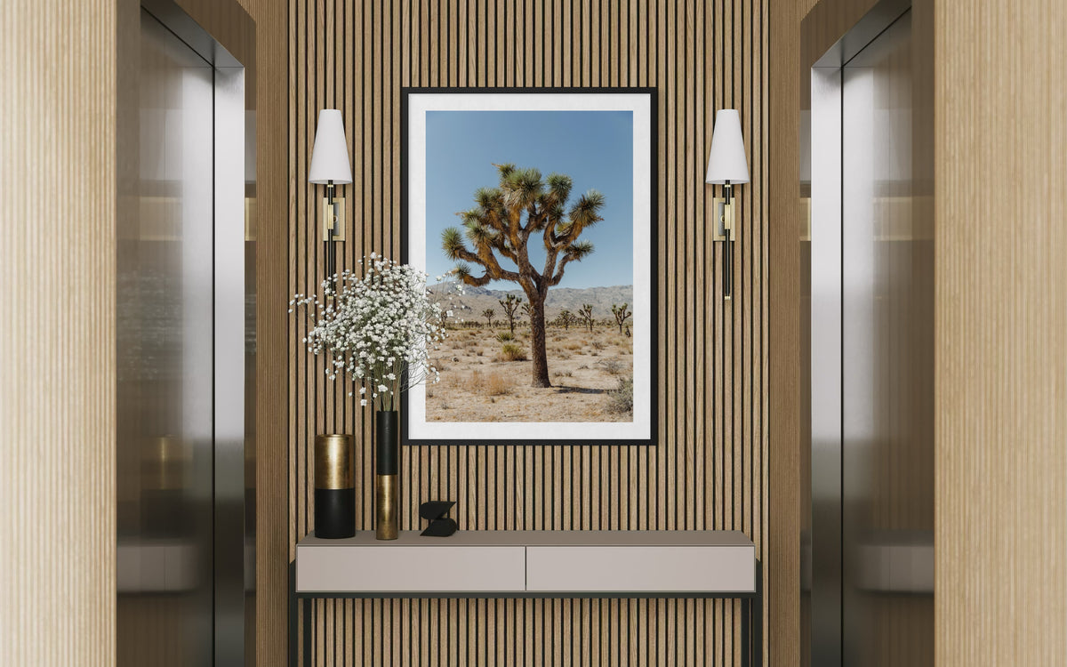 Framed photo of Joshua Tree in California desert, displayed above a console with vases between two elevators.