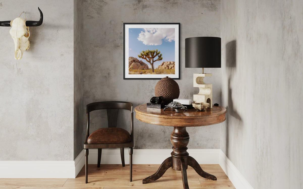 Framed Joshua Tree IV art on a gray wall above a round table with decor, lamp, and chair in a cozy corner.