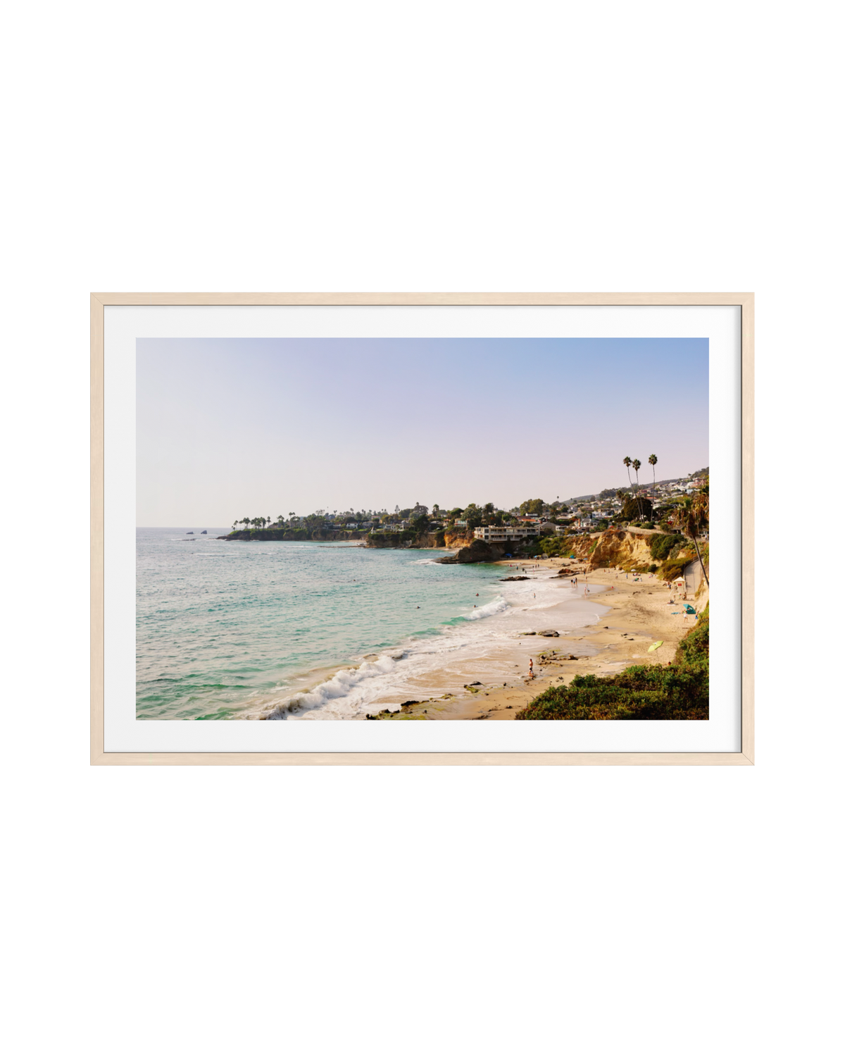 Pacific coastline at Laguna Beach with gentle waves, sandy coves, cliffs, palm trees, and homes in the distance.