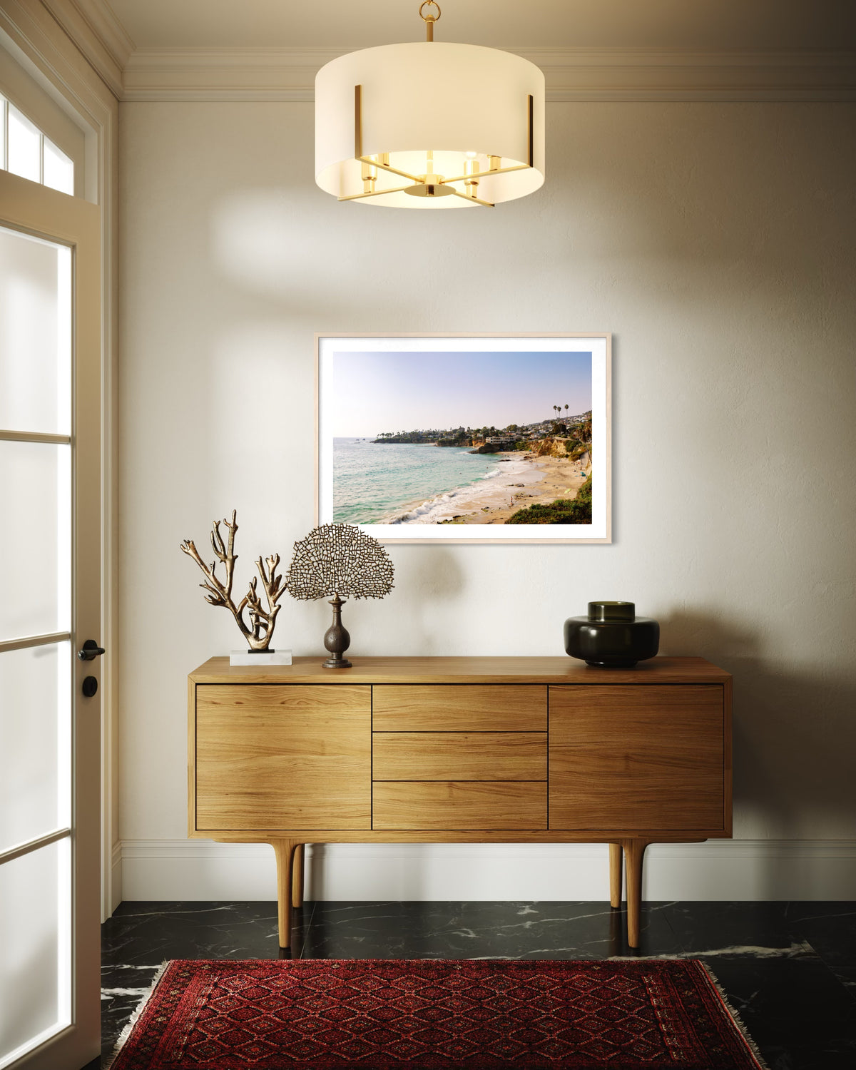 Laguna Beach ocean view photograph displayed above a wooden console in a modern entryway with a red rug.