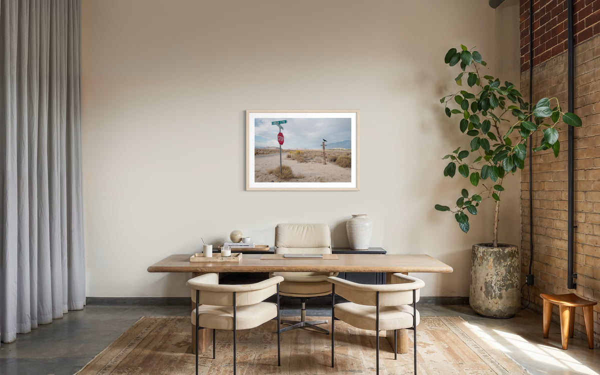 Wooden desk, two chairs, large plant, and “Lone Pine Sentinel” high desert photo wall art in minimalist office.