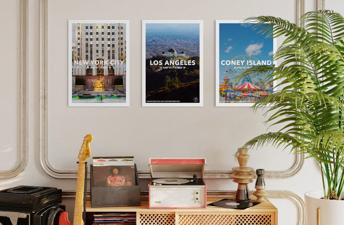 Los Angeles, New York City, and Coney Island poster set displayed above a record player, guitar, and houseplant.