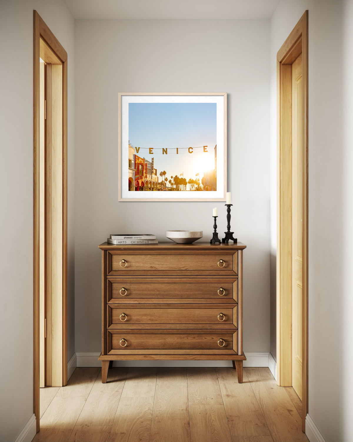 A wooden dresser in a hallway with books, a bowl, candle holders, and the “Magic Hour in Venice” photo displayed.