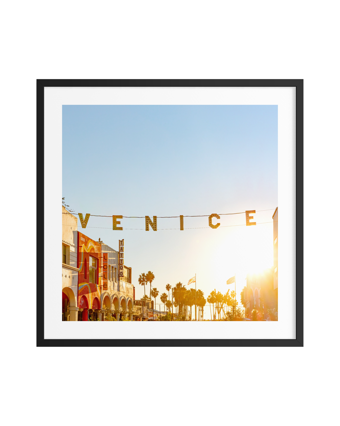 Venice street scene at dusk with a glowing sign, palm trees, and colorful buildings in a black frame.