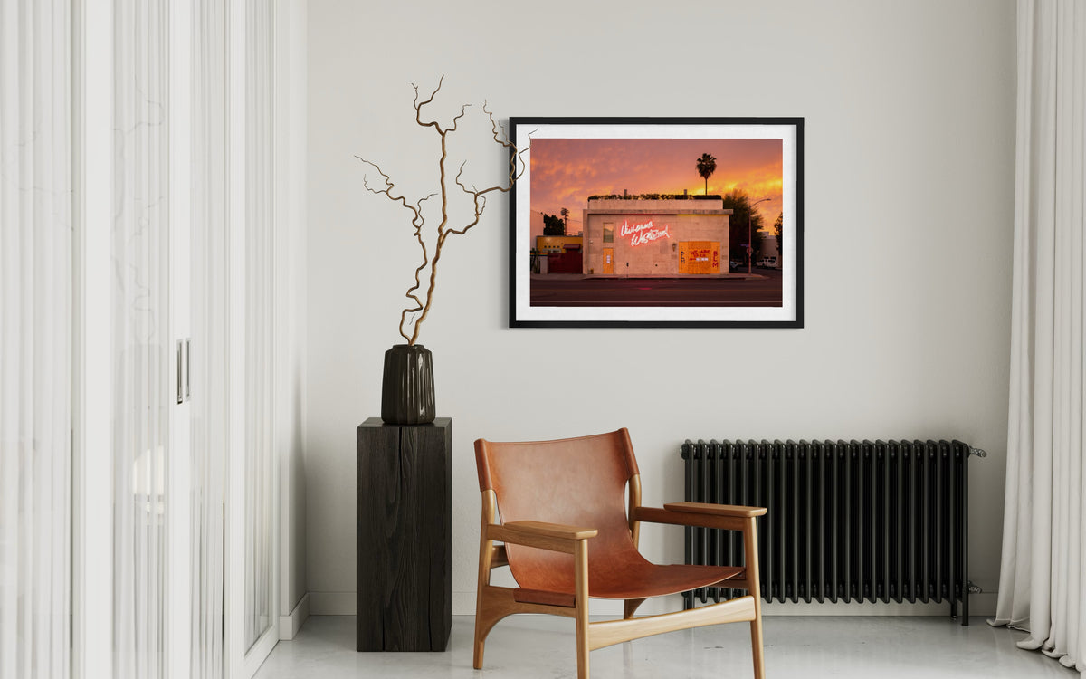Framed “Melrose Avenue, the Summer of 2020” print above radiator in a living room with leather chair and tall vase.
