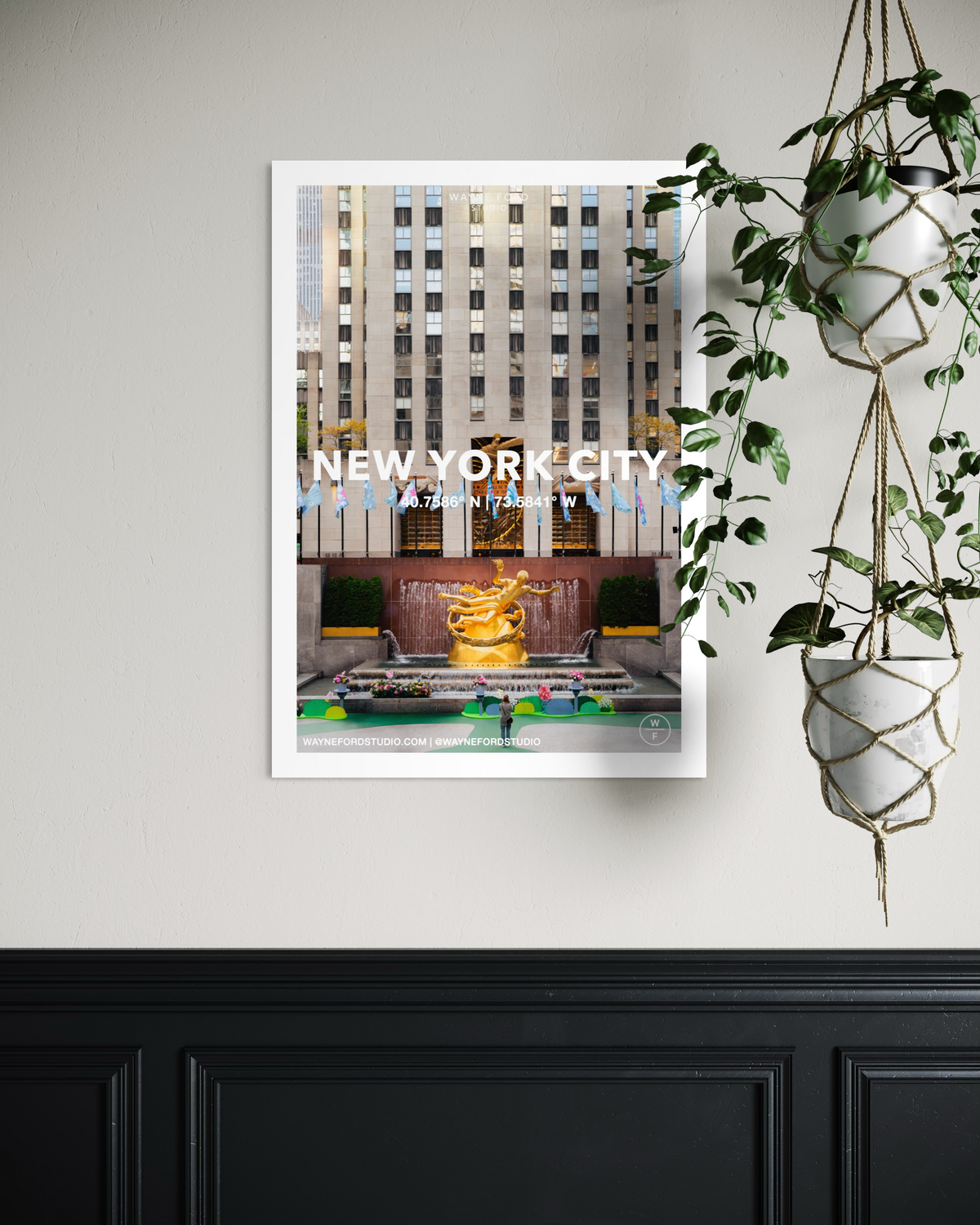 Framed New York City poster print displayed on a beige wall beside two white hanging planters with green plants.