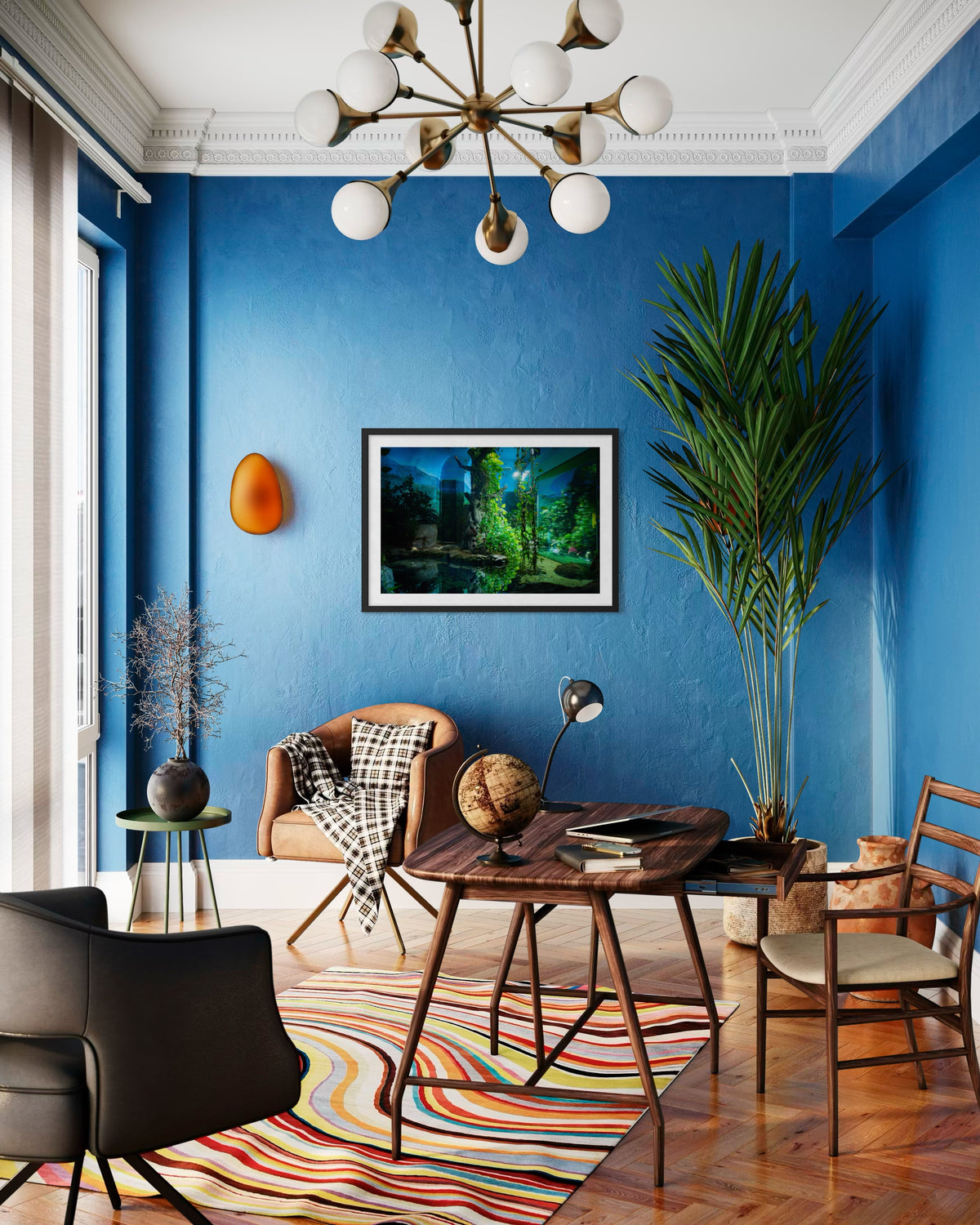 Blue-walled room at night with a desk, chairs, globe, plant, rug, and chandelier softly lit.